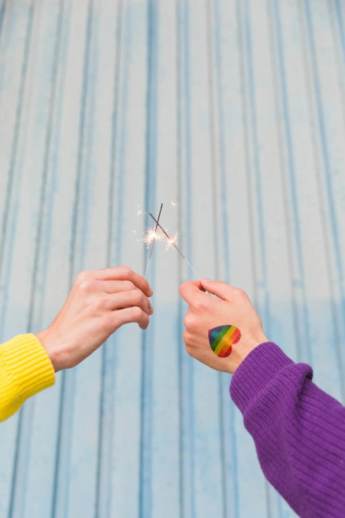 Hände von Menschen, die gekreuzte Bengallichter halten.